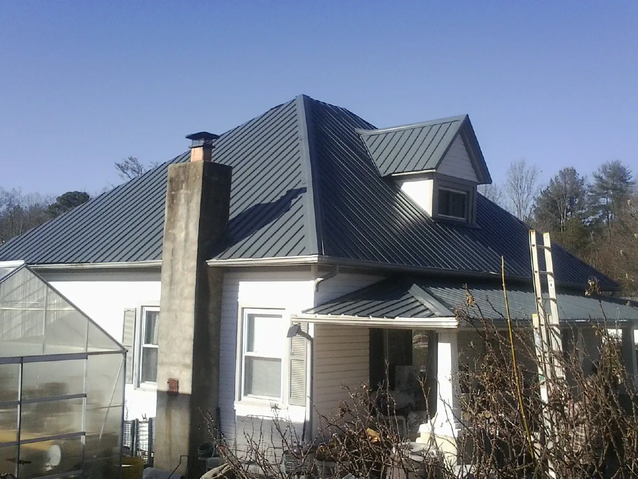 Dark blue standing seam metal roof on a white farmhouse with dormer — Slate & Tile Roof Repair by Roofing Brothers in Mc Kenney