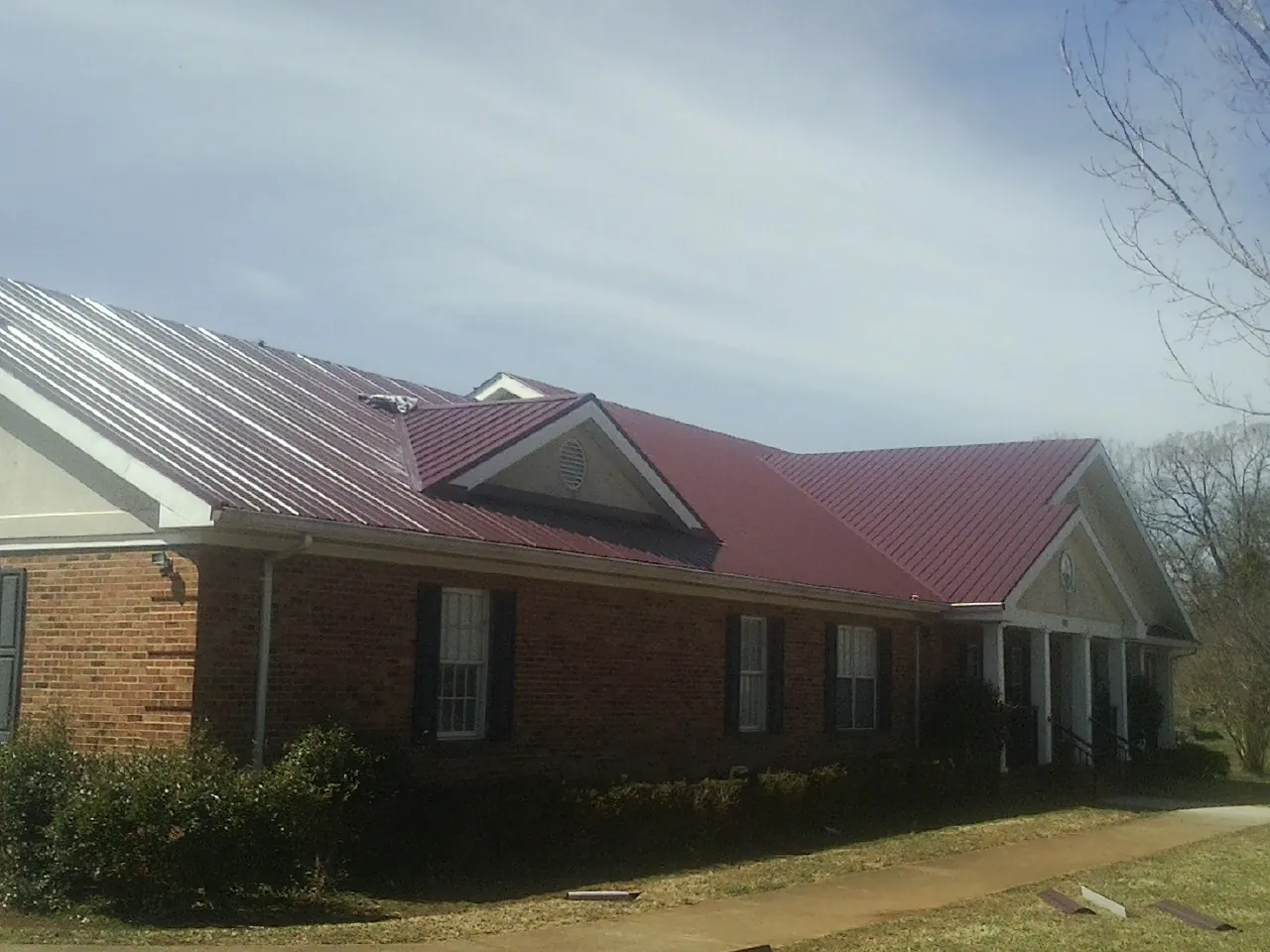 Red metal roof with gabled entries on a long brick building, from a Hail Damage Roof Repair job in Mc Kenney