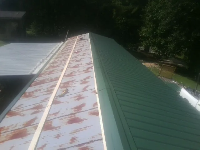 Old rusted panels beside newly installed green metal roofing — Wind Damage Roof Repair by Roofing Brothers in Mc Kenney