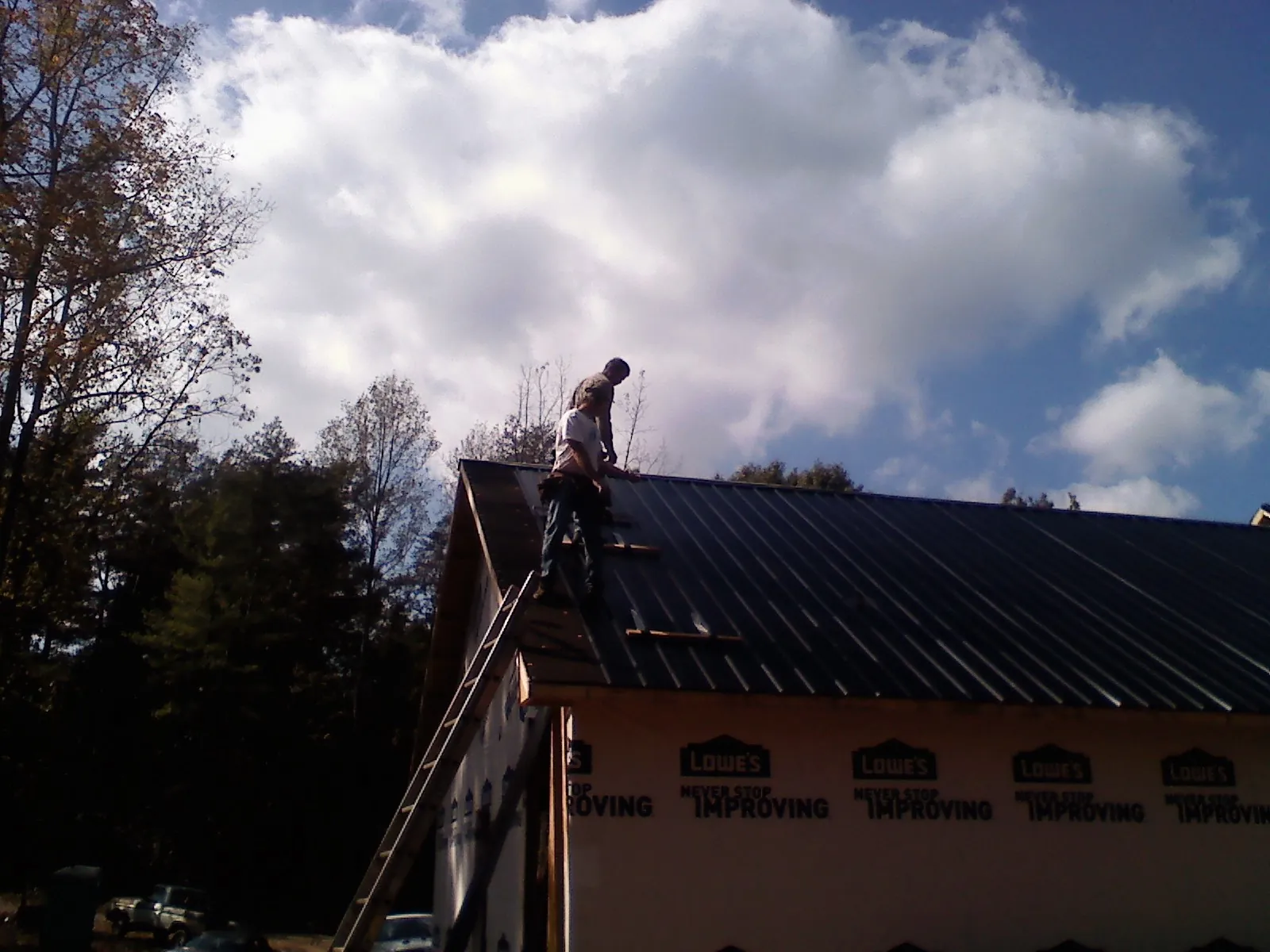 Roofer fastening dark metal panels high against a cloudy sky, from a Roof Inspection job in Mc Kenney