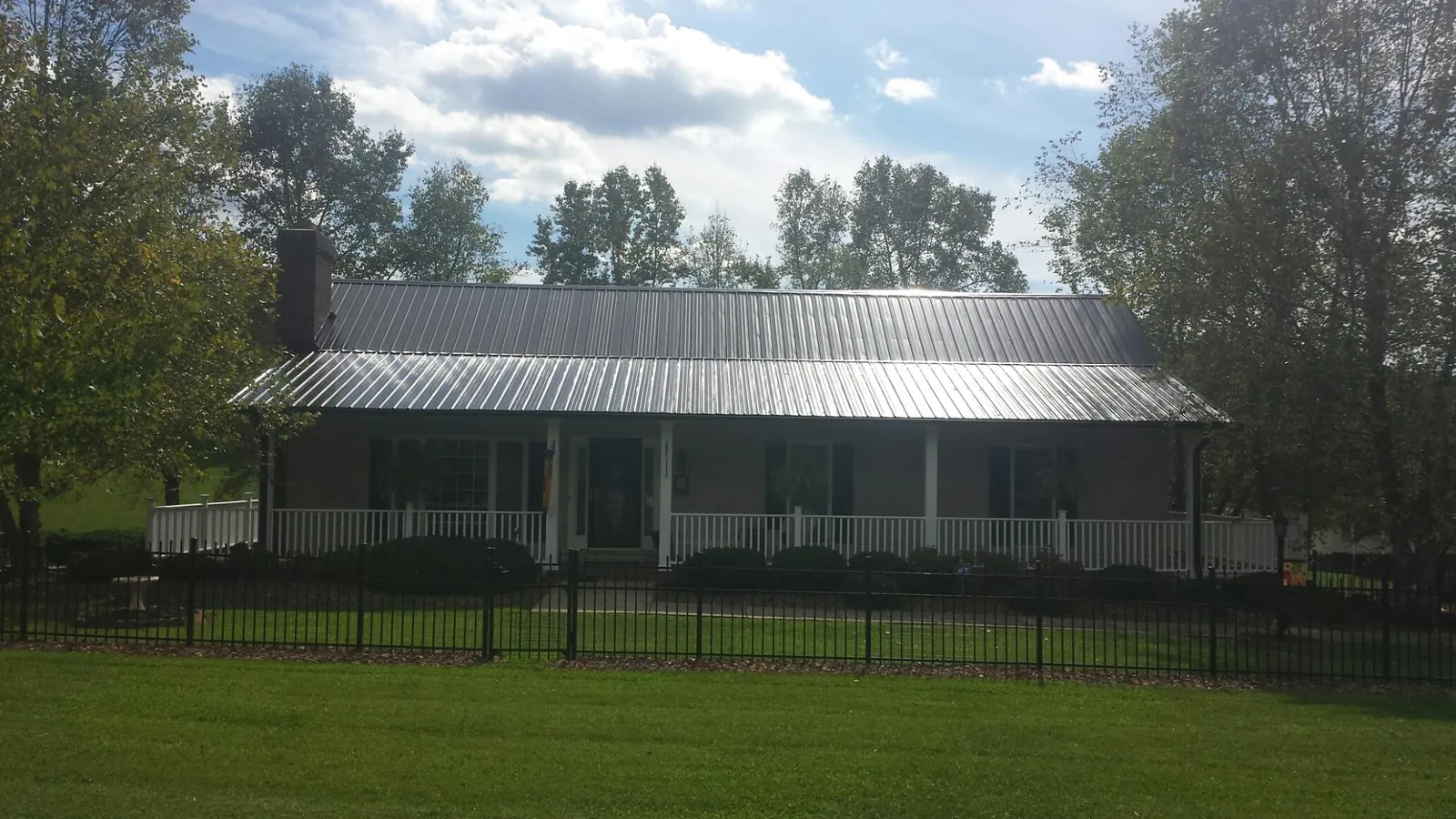 Gray metal roof on a brick ranch with a full width front porch — Gutter Guard Installation work by our crew in Mc Kenney