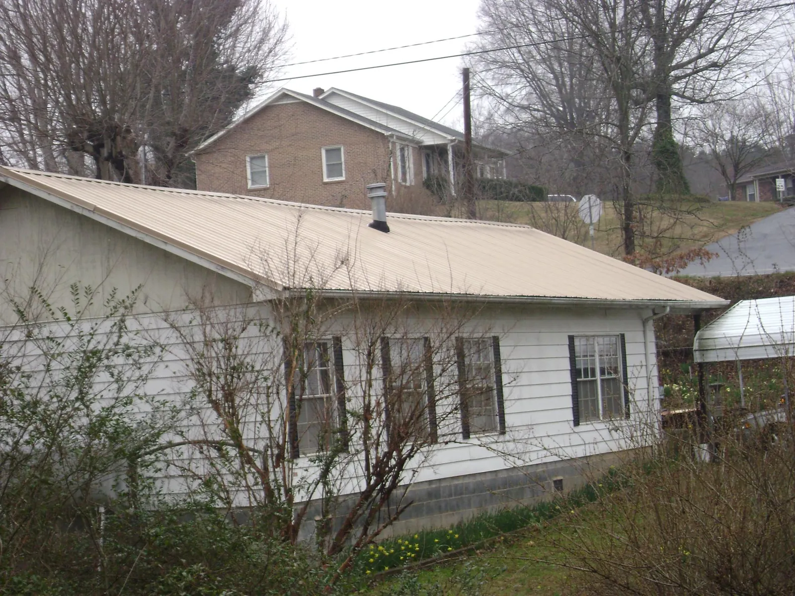Tan metal roof on a white sided house set into a hillside — Commercial Roofing by Roofing Brothers in Mc Kenney