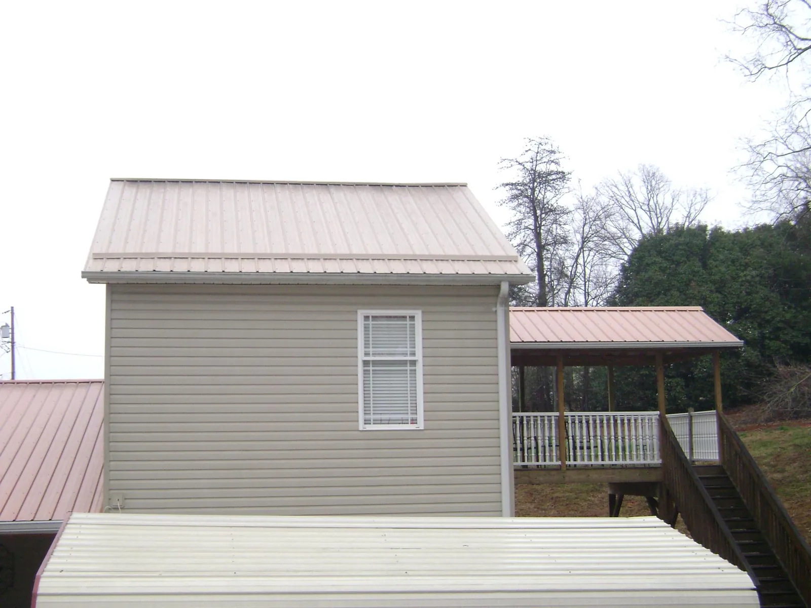 Tan metal roofs on a two story addition and attached porch, from a Roof Replacement job in Mc Kenney